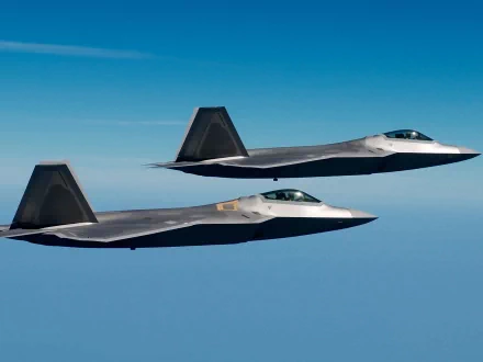 Two Lockheed Martin F-22 Raptors flying in formation against a clear blue sky, captured in a high-definition desktop wallpaper and background image.