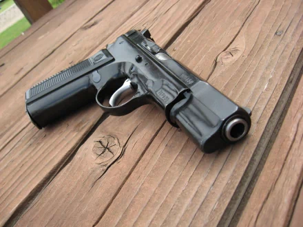 A high-definition desktop wallpaper featuring a black pistol resting on a wooden surface.