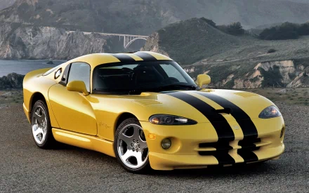 A high-definition wallpaper of a yellow Dodge Viper with black stripes, parked on a scenic coastal road with mountains in the background.