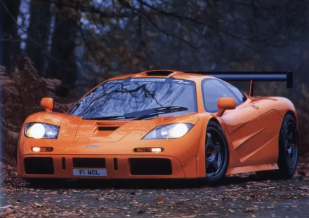 HD desktop wallpaper of an orange McLaren F1 vehicle, showcasing its sleek design in an outdoor setting with autumn foliage and a misty atmosphere in the background.