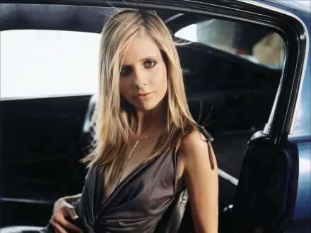 HD desktop wallpaper featuring celebrity Sarah Michelle Gellar seated in a car, exuding elegance with her blonde hair and deep neckline outfit.