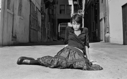 A striking black and white image of Shannyn Sossamon sitting in an alley, wearing a stylish outfit, capturing a moody and artistic vibe. This serves as a captivating HD desktop wallpaper.