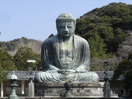 An HD desktop wallpaper depicting a serene statue of Buddha in a peaceful outdoor setting, surrounded by lush greenery. The image has religious and Buddhist significance.