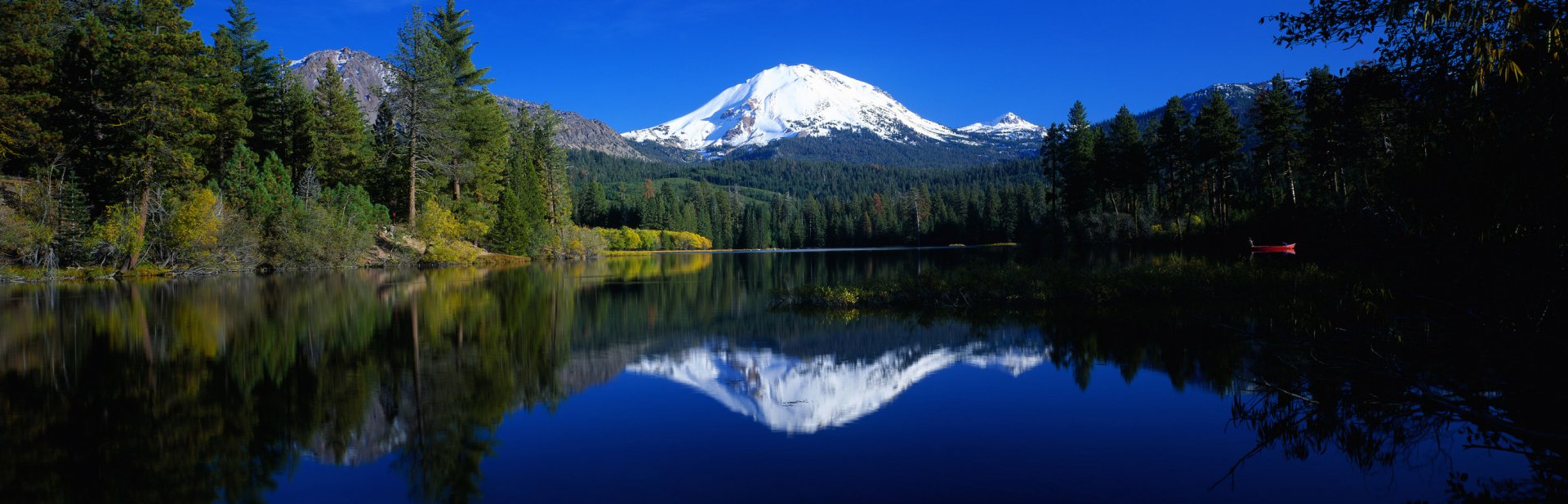 HD desktop wallpaper featuring a stunning view of Lake Tahoe with a snow-capped mountain in the background, surrounded by lush greenery and forest, reflecting perfectly in the clear blue lake water.