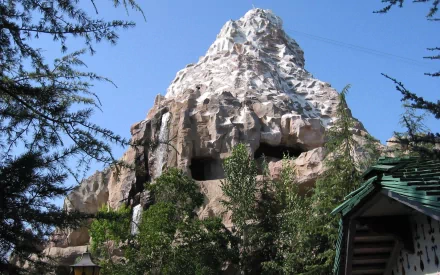 A striking view of the Matterhorn at Disneyland, surrounded by lush greenery, captured in an HD desktop wallpaper, showcasing the iconic man-made mountain under a clear blue sky.