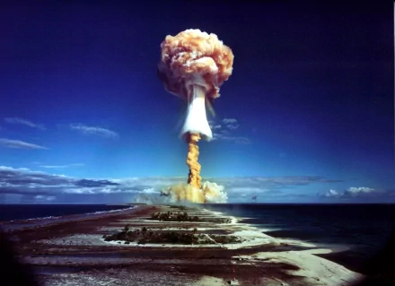 HD desktop wallpaper showing a dramatic explosion over an island with a towering mushroom cloud, under a clear blue sky. Military and explosive themes dominate the vivid imagery.
