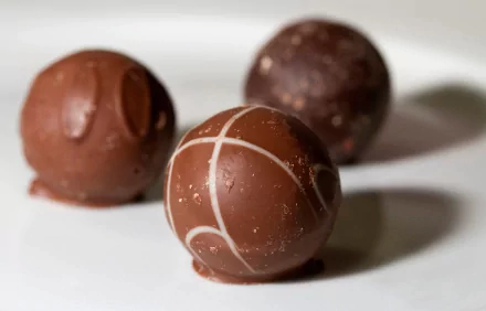 Three chocolate truffles on a white surface, featured in an HD desktop wallpaper and background.