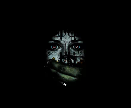 A dark and scary HD desktop wallpaper, featuring a face with eerie eyes and intricate designs, partially covered by a green, sinister hand.