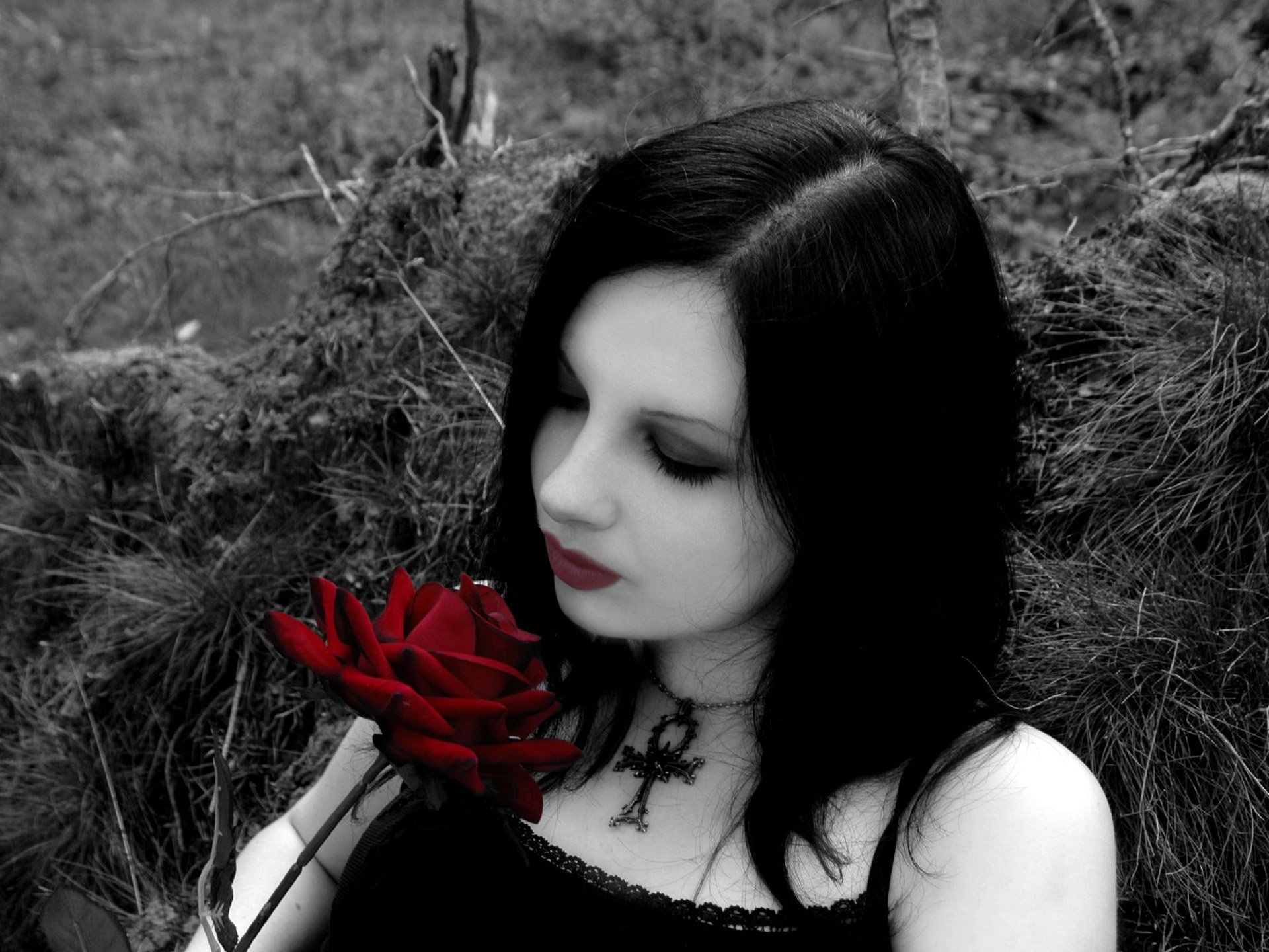 HD wallpaper of a celebrity, Michelle Trachtenberg, with black hair and dark makeup, holding a red rose. The background is monochrome and she wears a black cross necklace.