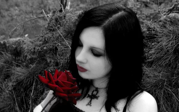 HD wallpaper of a celebrity, Michelle Trachtenberg, with black hair and dark makeup, holding a red rose. The background is monochrome and she wears a black cross necklace.