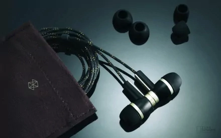 HD desktop wallpaper featuring a close-up of a man-made Zune earphones with ear tips and a fabric pouch on a reflective surface.