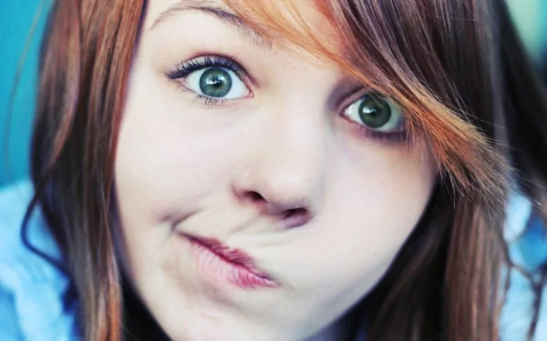A close-up of a woman with striking green eyes and playful lips, framed by flowing hair, exuding a whimsical mood. This HD image serves as an engaging desktop wallpaper.