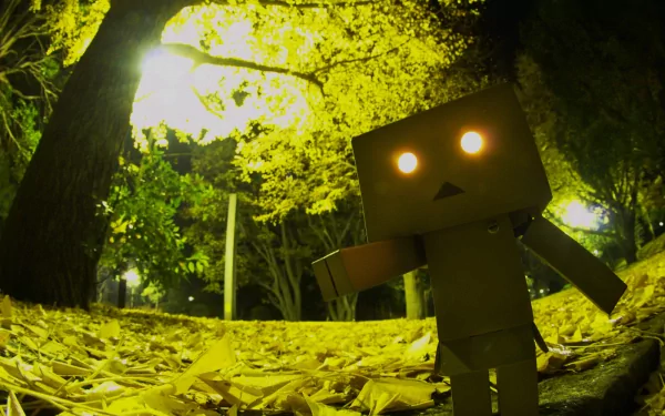 A whimsical Danbo figure stands amidst golden autumn leaves under soft lighting, creating a charming atmosphere for this HD desktop wallpaper.