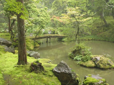 HD desktop wallpaper of a serene garden featuring a stream, moss-covered rocks, and a man-made bridge surrounded by lush trees.