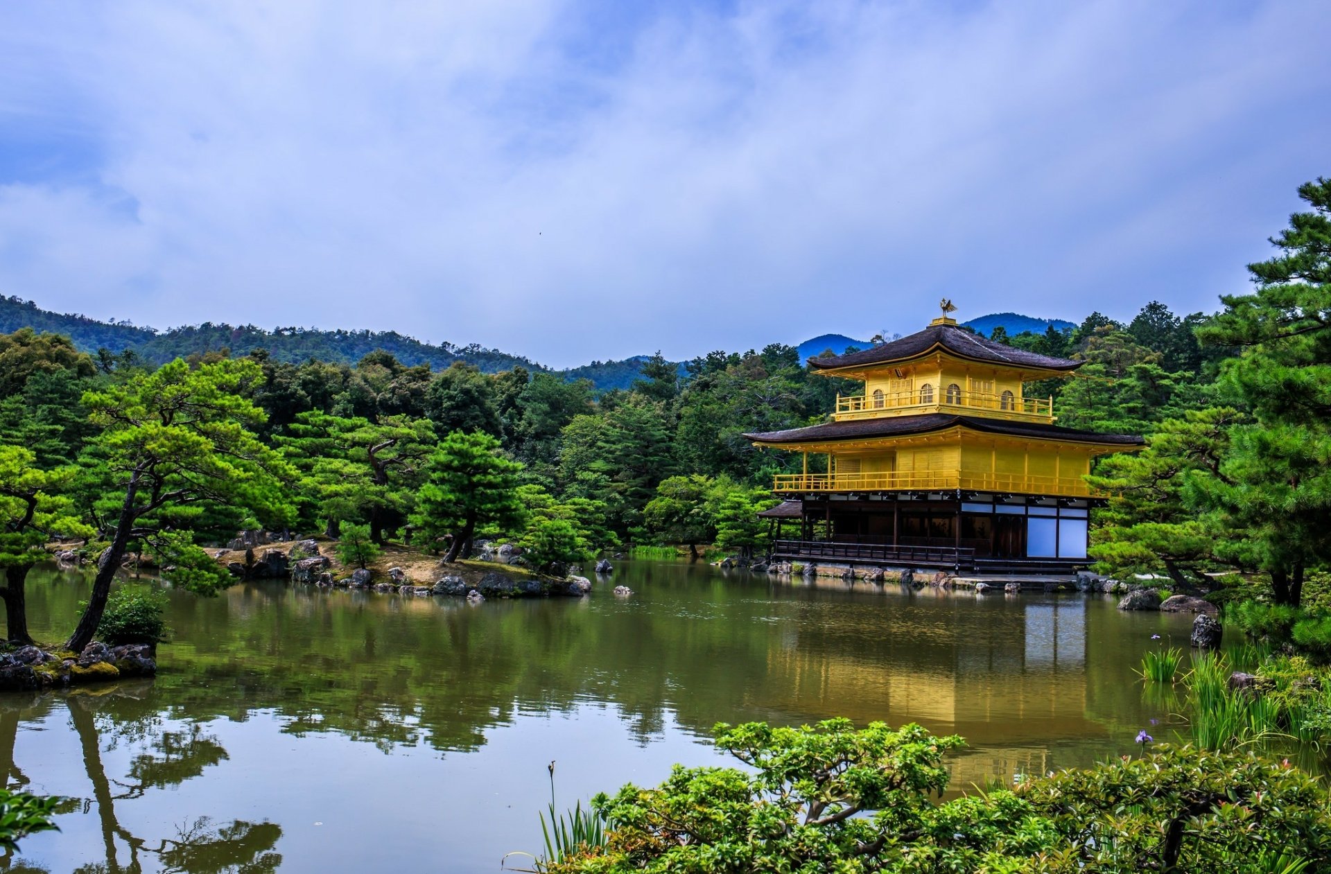 HD desktop wallpaper of Kinkaku-ji (Golden Pavilion) in Kyoto, Japan, reflected in a tranquil pond amid wooded hills and temple gardens, a religious Zen landmark.