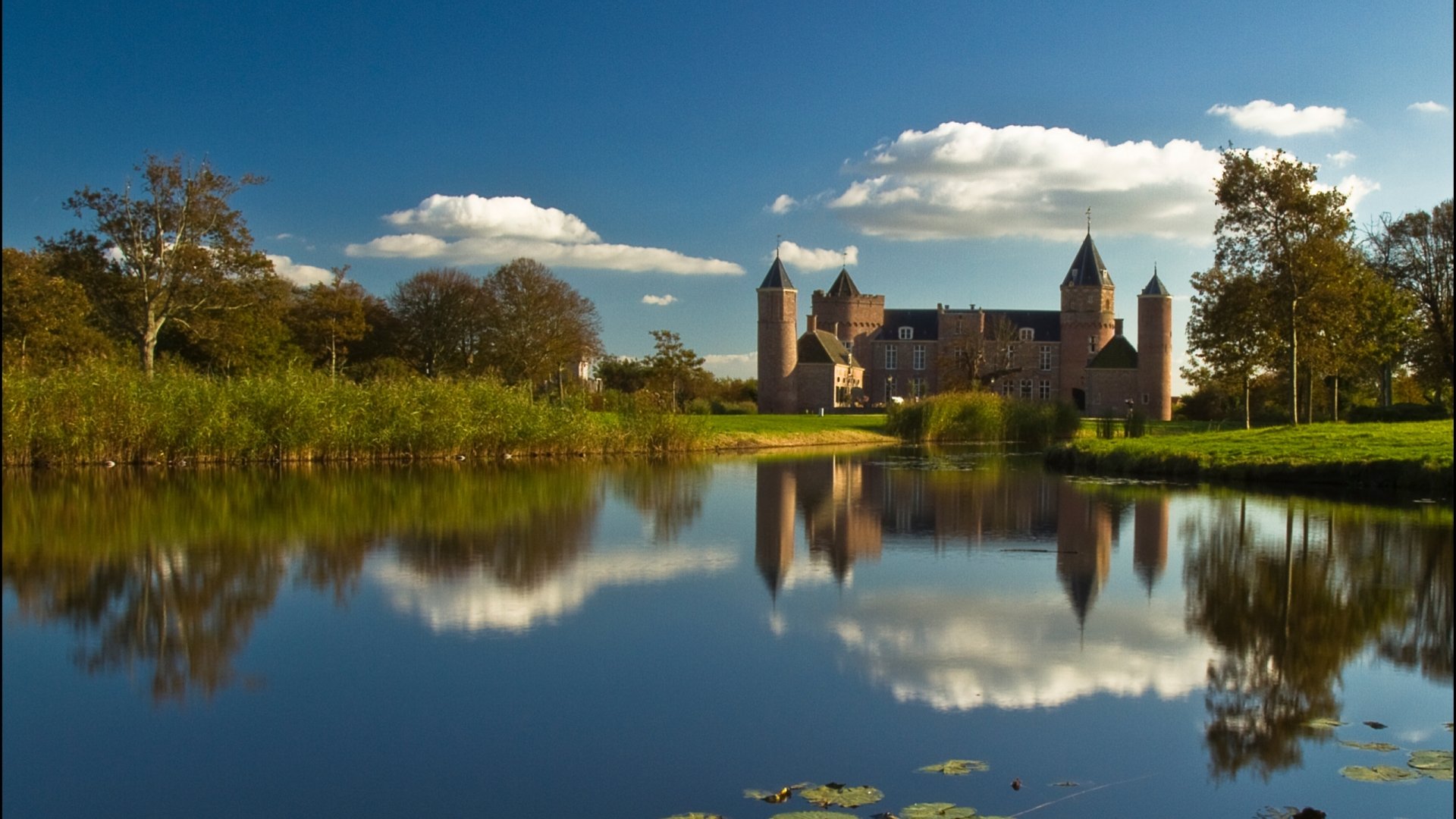 HD desktop wallpaper featuring the man-made Westhove Castle reflected in a calm body of water under a blue sky with scattered clouds.