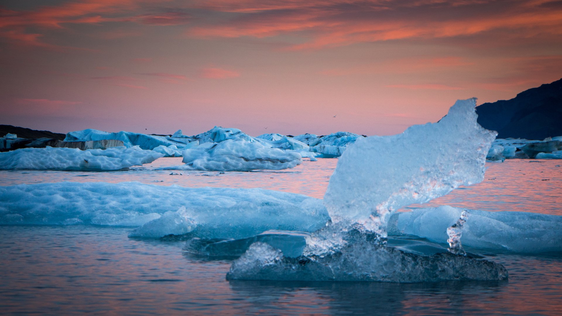 4K Ultra HD desktop wallpaper showcasing a serene iceberg landscape at sunset with soft pink and orange hues reflecting on the calm water.