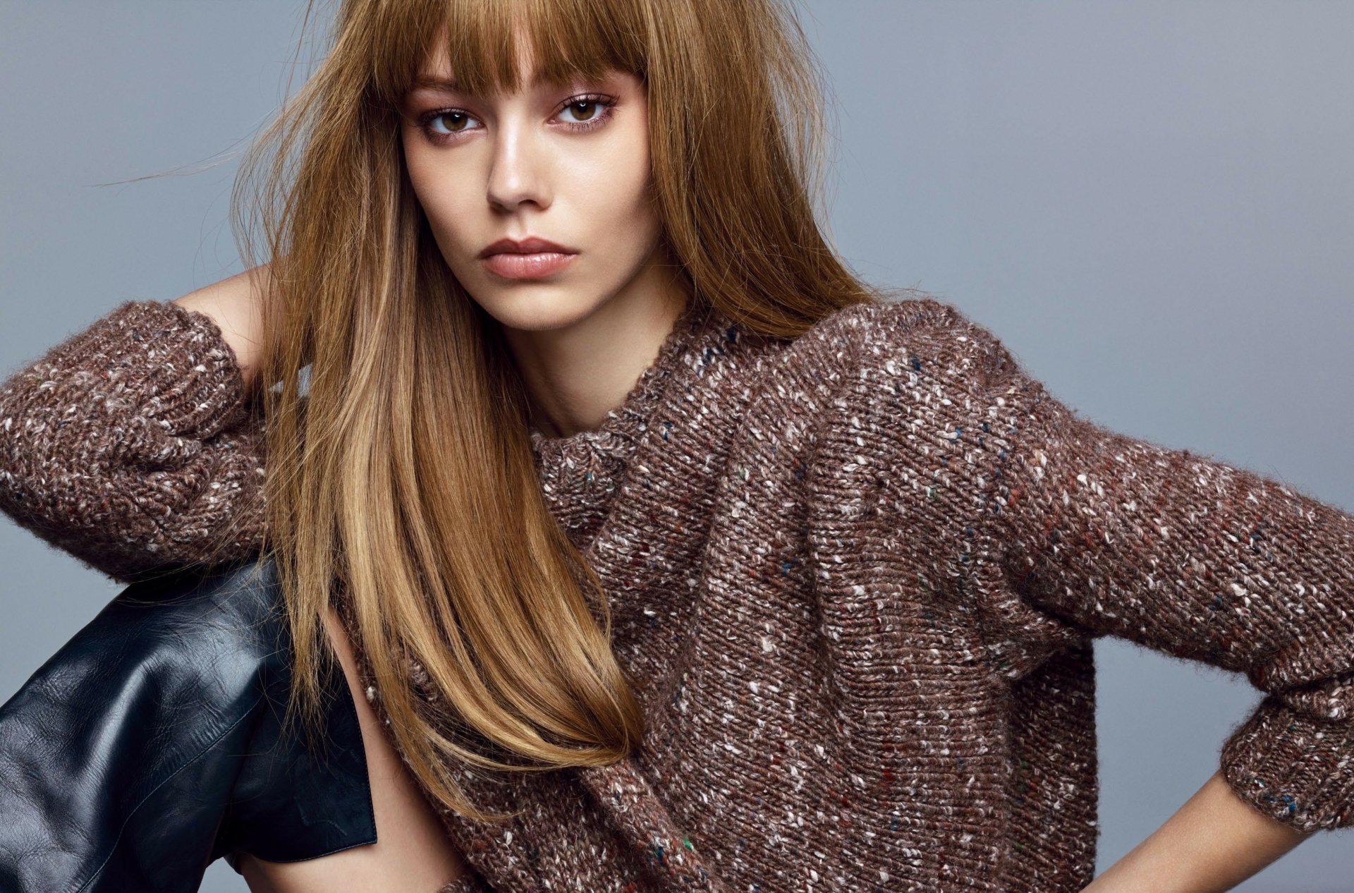 Woman with long light brown hair wearing a textured brown sweater, seated against a soft gray backdrop — 2K Quad HD PC desktop wallpaper and background.