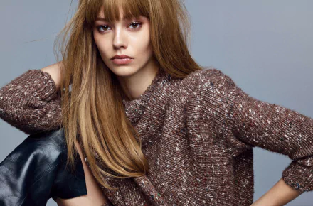 Woman with long light brown hair wearing a textured brown sweater, seated against a soft gray backdrop — 2K Quad HD PC desktop wallpaper and background.