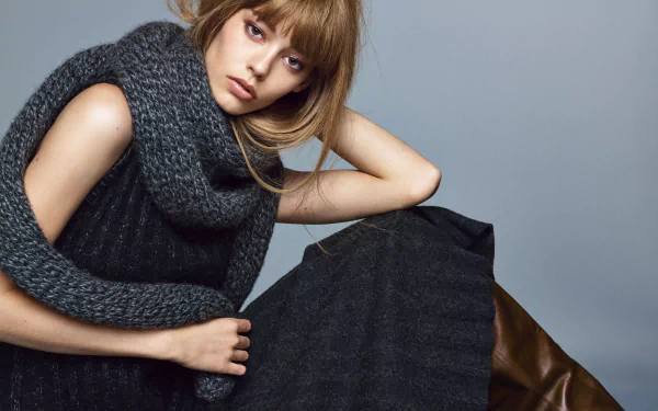 HD desktop wallpaper of a woman with light brown hair wearing a chunky gray scarf and black outfit against a plain gray background.