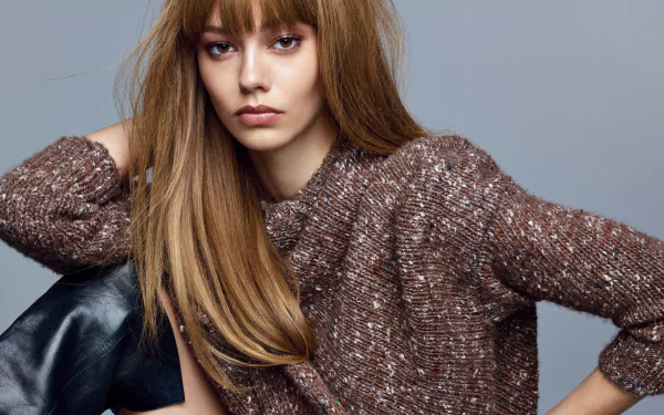 Woman with long light brown hair wearing a textured brown sweater, seated against a soft gray backdrop — 2K Quad HD PC desktop wallpaper and background.