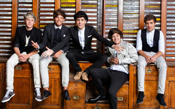 A vibrant HD desktop wallpaper featuring the members of One Direction, posed together, radiating charisma against a backdrop of catalog drawers, embodying a dynamic music moment.