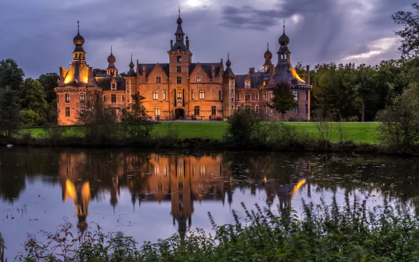 Man-made Ooidonk Castle illuminated at dusk, mirrored in a calm moat — 2K Quad HD PC desktop wallpaper/background.
