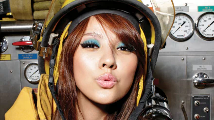 Close-up of a female pop singer in a yellow hood, puckering lips amid industrial gauges — vibrant HD PC desktop wallpaper/background that evokes music and glam.