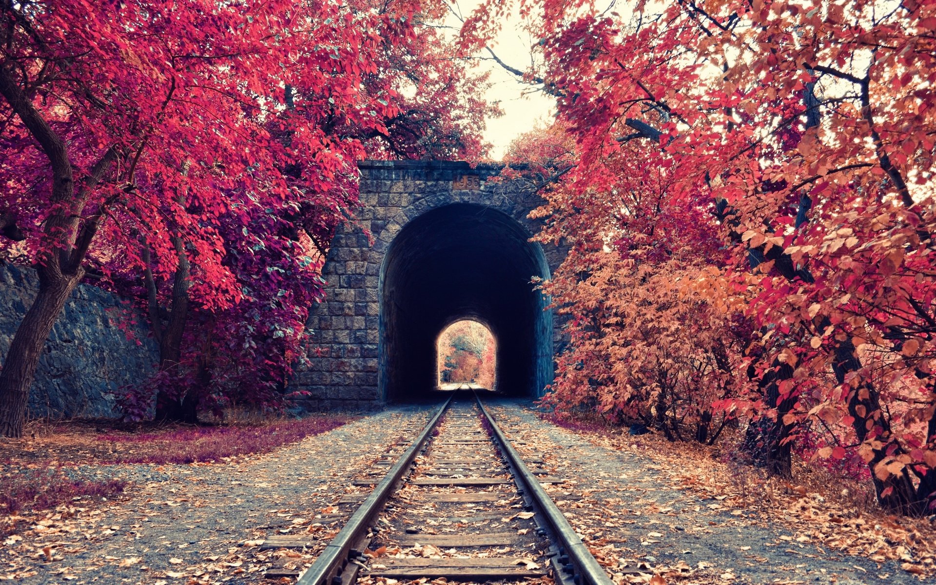 HD desktop wallpaper of a man-made railroad leading through a stone tunnel surrounded by vibrant autumn trees with red and orange foliage.