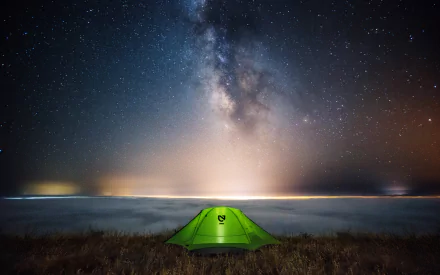 A green tent sits in a grassy field under a stunning starry sky, showcasing the Milky Way, creating a serene camping atmosphere in this HD desktop wallpaper.