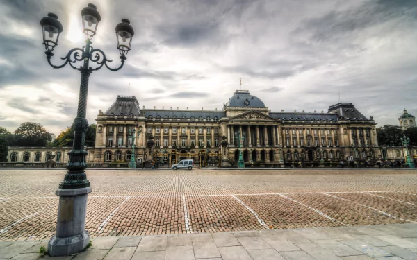 HD desktop wallpaper of the man-made Royal Palace of Brussels under a dramatic cloudy sky, ornate lamppost in the foreground and a wide cobblestone plaza.
