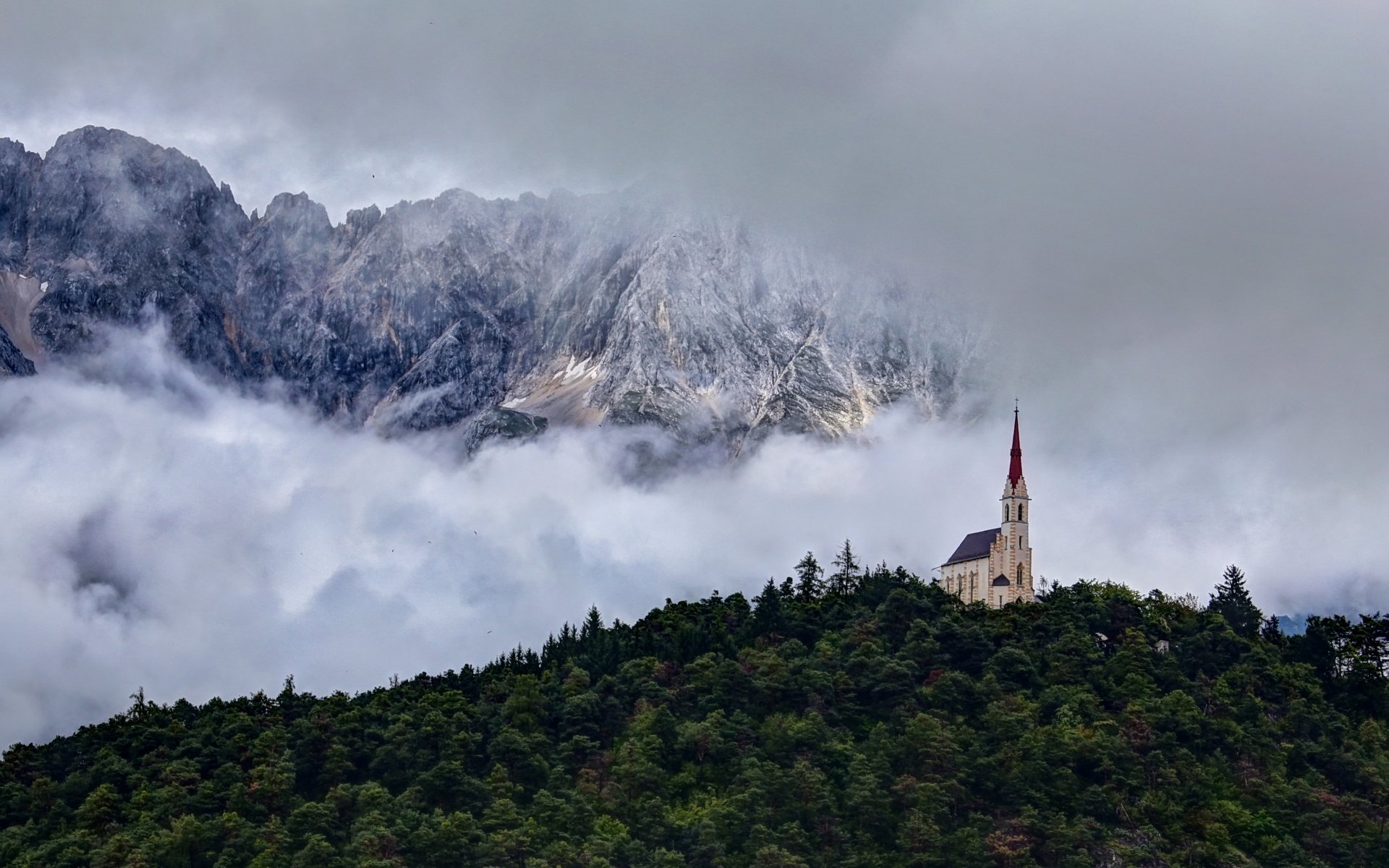 HD PC desktop wallpaper showing a serene church perched on a forested hill with misty mountains in the background, evoking a peaceful religious atmosphere.