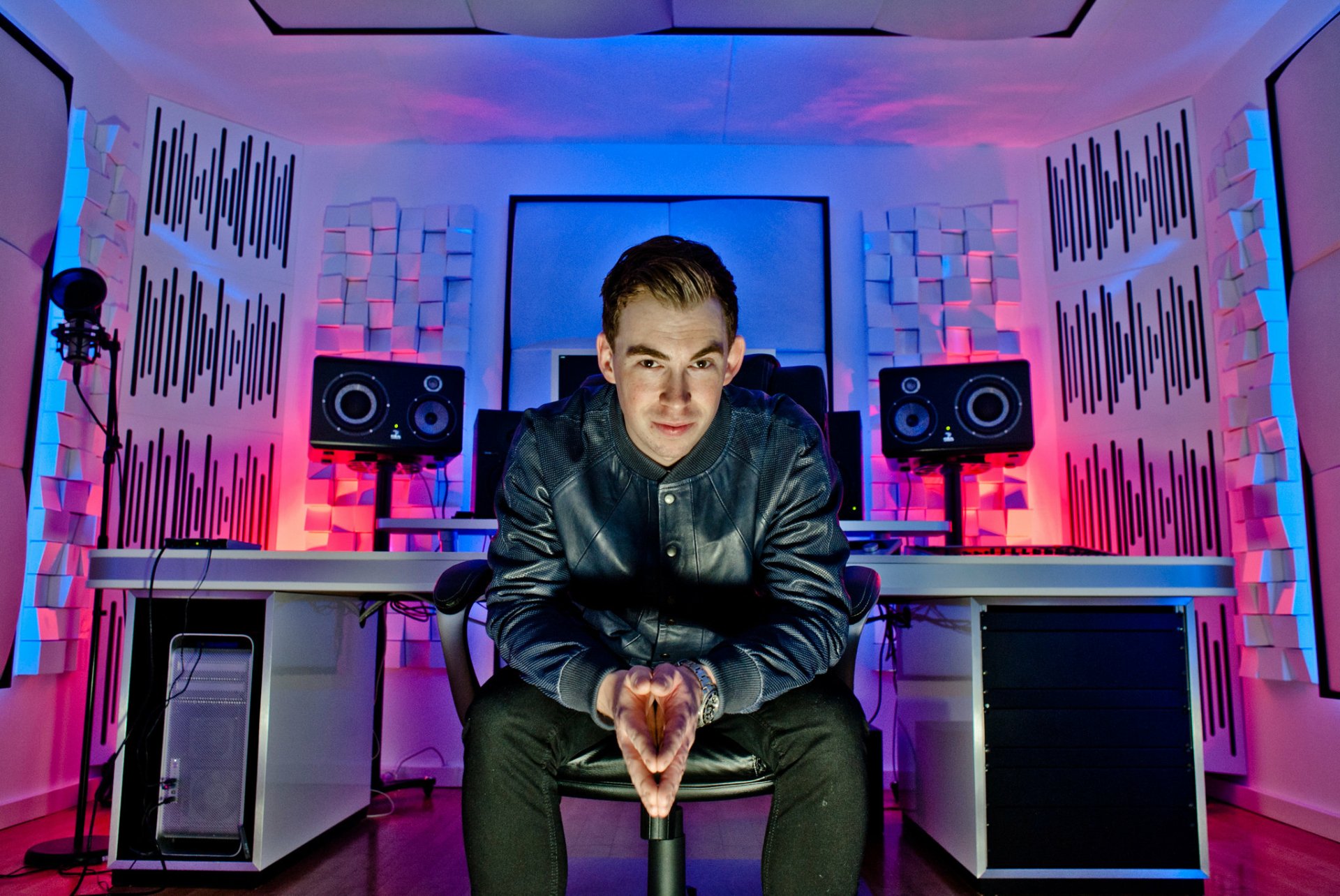 HD PC desktop wallpaper of Hardwell in a music studio with vibrant blue and pink lighting, surrounded by speakers and acoustic panels.