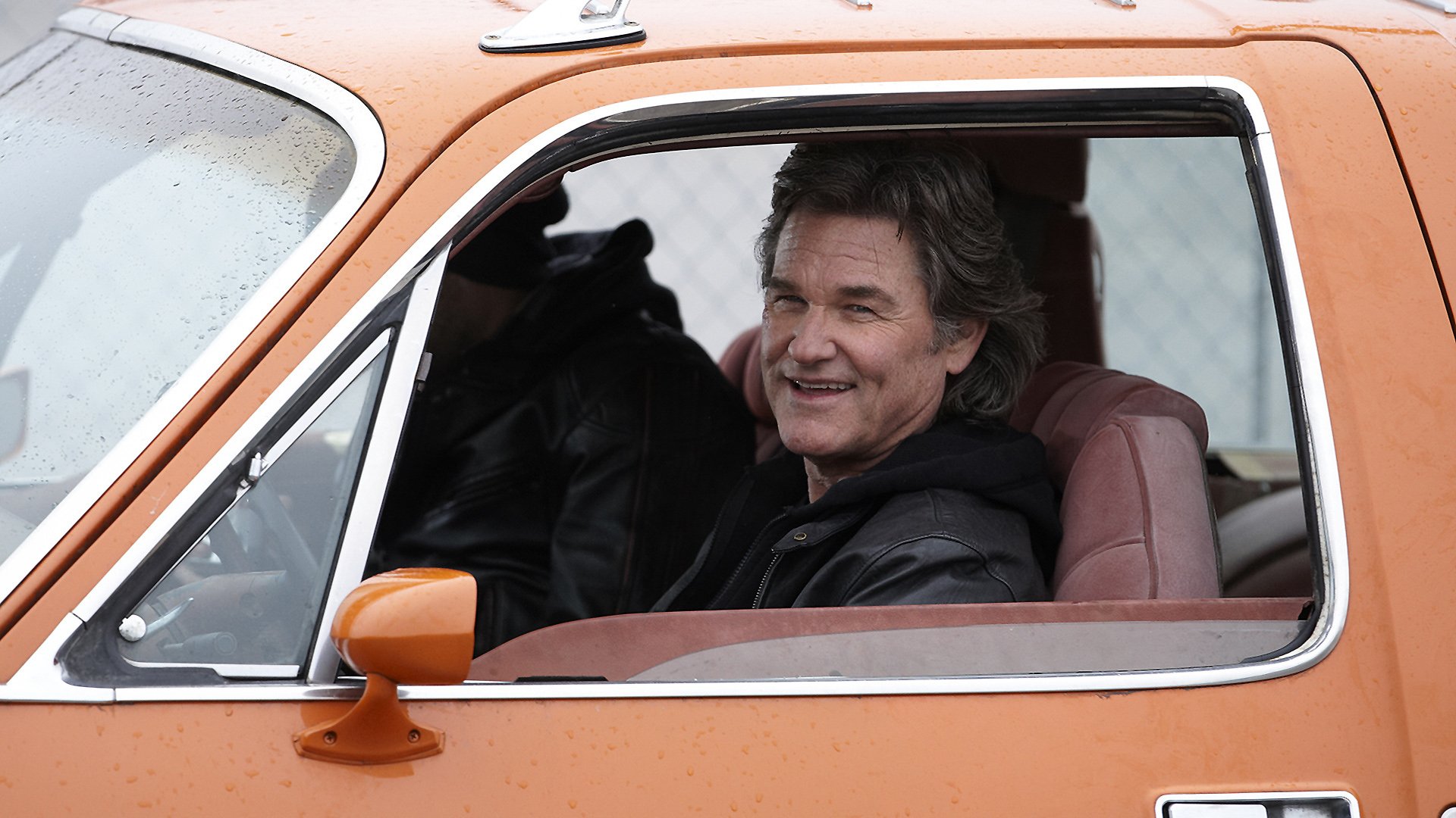 HD PC desktop wallpaper background from the movie The Art Of The Steal showing a smiling man in the driver's seat of an orange vintage car, looking out the open window.