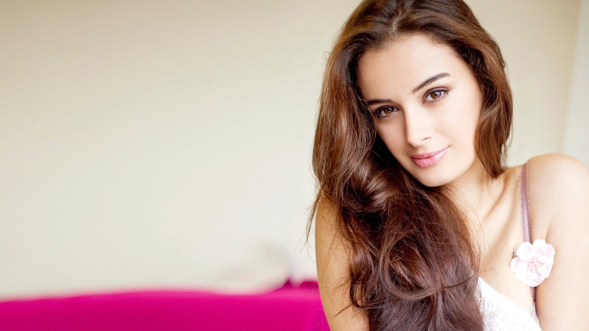A stunning HD desktop wallpaper featuring celebrity Evelyn Sharma, showcasing her long, flowing hair and captivating smile against a soft, pink background.