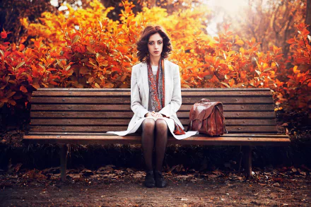 A woman sits on a bench surrounded by vibrant fall foliage in Bordeaux, France, captured in an HD desktop wallpaper showcasing autumn's rich colors and a reflective mood.