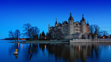 Evening view of Schwerin Palace in Germany, a majestic man-made castle reflected in calm waters against a clear blue sky, captured as a HD PC desktop wallpaper.
