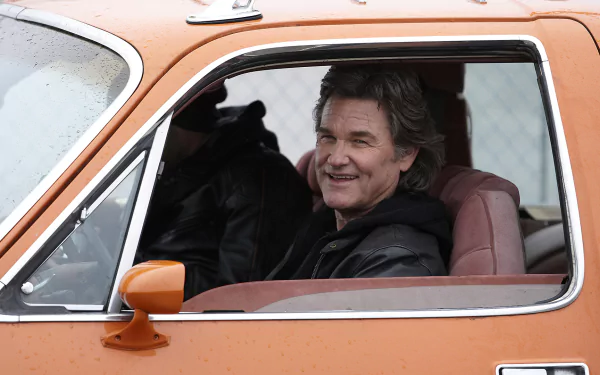 HD PC desktop wallpaper background from the movie The Art Of The Steal showing a smiling man in the driver's seat of an orange vintage car, looking out the open window.