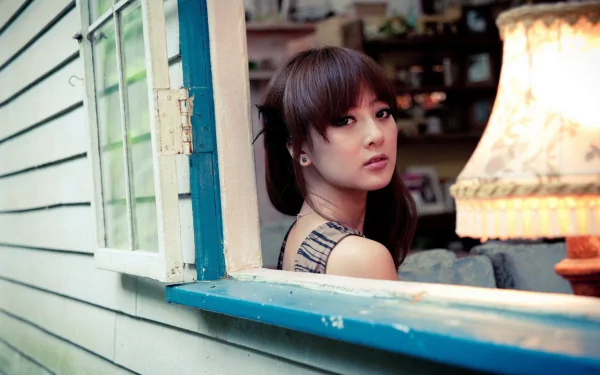 A Taiwanese woman sits by an open window in a cozy room decorated with shelves and a stylish lamp in this HD desktop wallpaper featuring Mikako Zhang Kaijie.