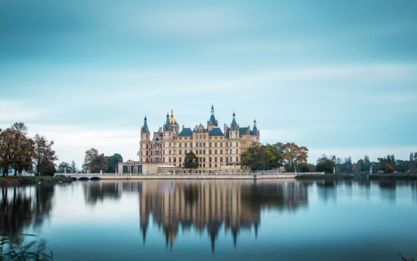 HD desktop wallpaper featuring Schwerin Palace reflected in calm water under a serene sky, showcasing man-made architectural beauty.