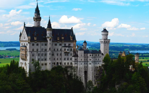 Neuschwanstein Castle in Germany perched on a forested hill under a bright blue sky — 5K Ultra HD PC desktop wallpaper and background.