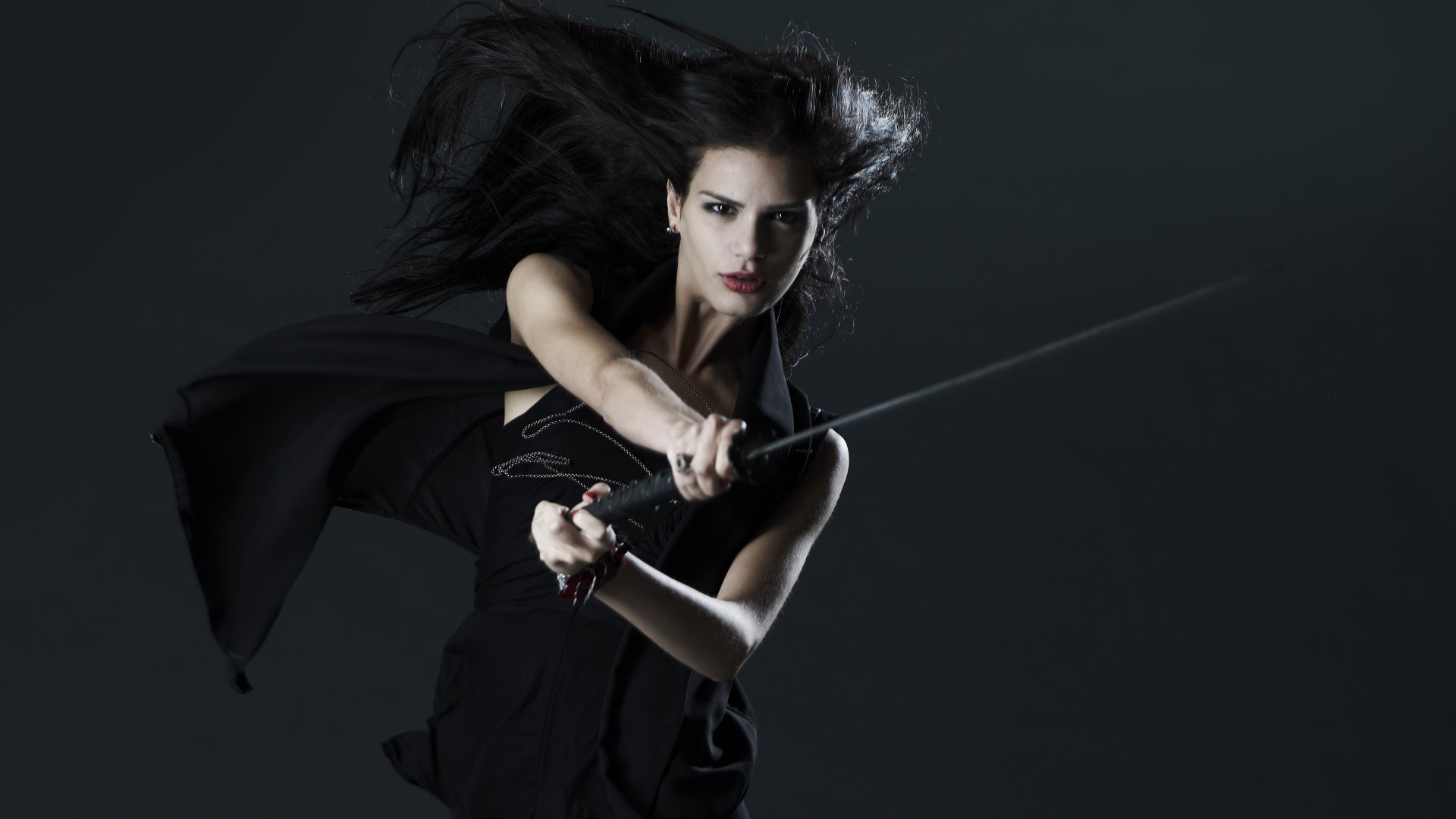 A fierce woman warrior wields a sword, her hair flowing dramatically against a dark backdrop, capturing the essence of fantasy in this 4K Ultra HD desktop wallpaper.