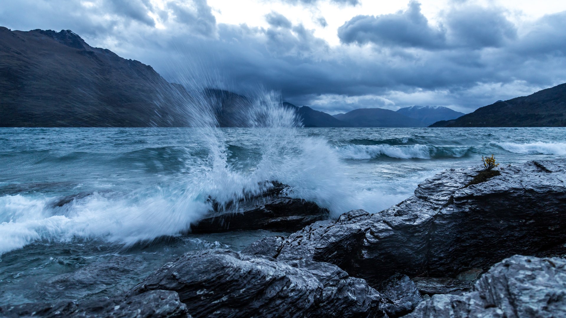 4K Ultra HD PC desktop wallpaper/background: nature ocean scene with waves crashing on a rocky shore beneath brooding clouds and distant mountain peaks.