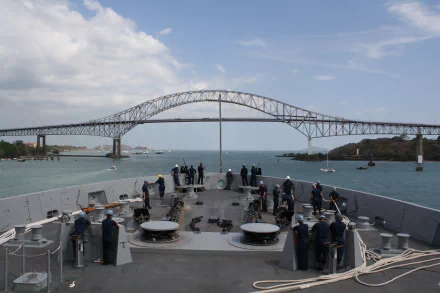 Bow view from US Navy amphibious transport dock USS San Diego (LPD-22) passing under the Bridge of the Americas, crew on deck and open sea beneath a blue sky — 2K desktop wallpaper