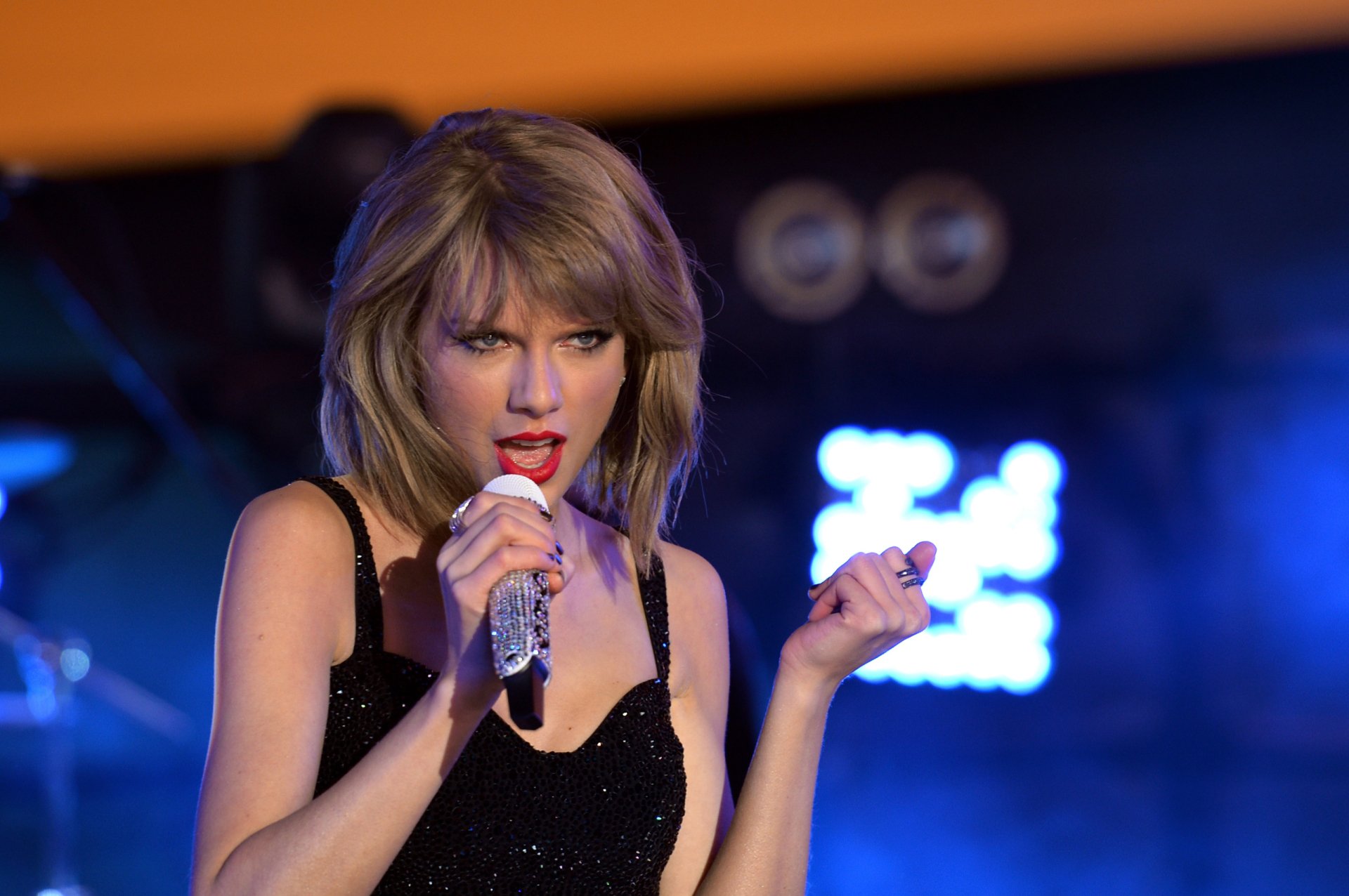 A dynamic HD desktop wallpaper featuring Taylor Swift performing passionately on stage, surrounded by vibrant stage lights, capturing the essence of her music.