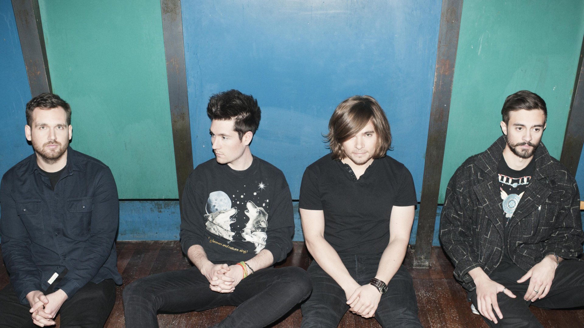 HD desktop wallpaper featuring the English rock band Bastille, with all four members seated against a blue and teal background.