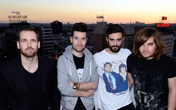 HD desktop wallpaper featuring the English rock band Bastille posing together against a cityscape at sunset, capturing their music and style.