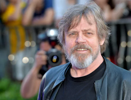 HD desktop wallpaper featuring a smiling Mark Hamill in a black outfit with a camera in the background.