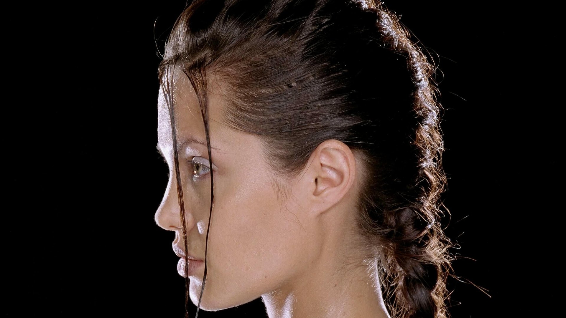 Close-up side profile of a braided woman against a black background, styled as Lara Croft: Tomb Raider — a 2K Quad HD PC desktop wallpaper and background.