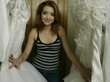 Alyson Hannigan poses in a casual striped tank top amidst elegant white dresses, creating a stylish atmosphere in this HD desktop wallpaper.